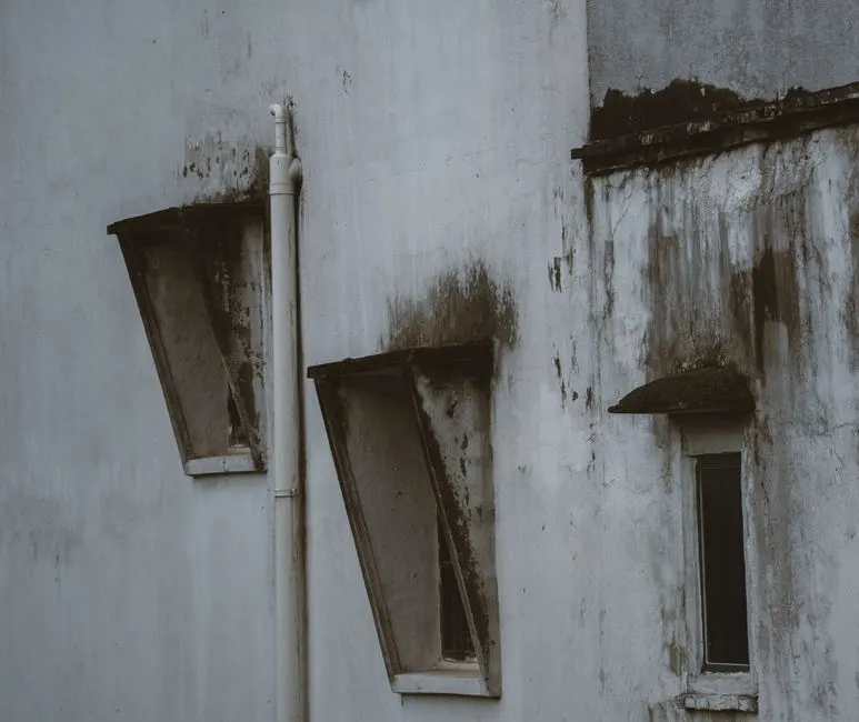 Close-up of a weathered building facade featuring rustic, tilted windows and peeling paint.